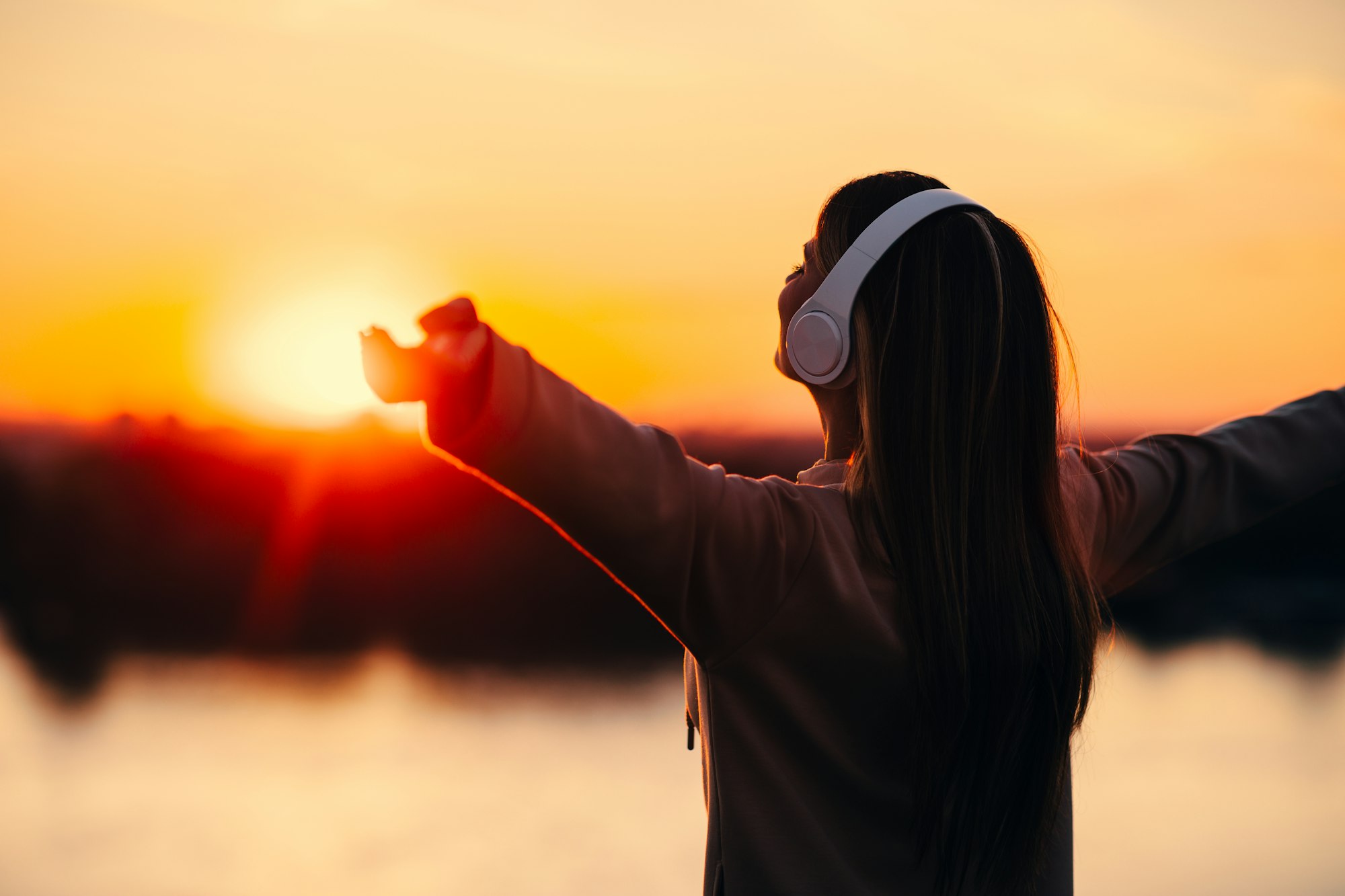 Young woman watching the sunset while listening to music via headphones